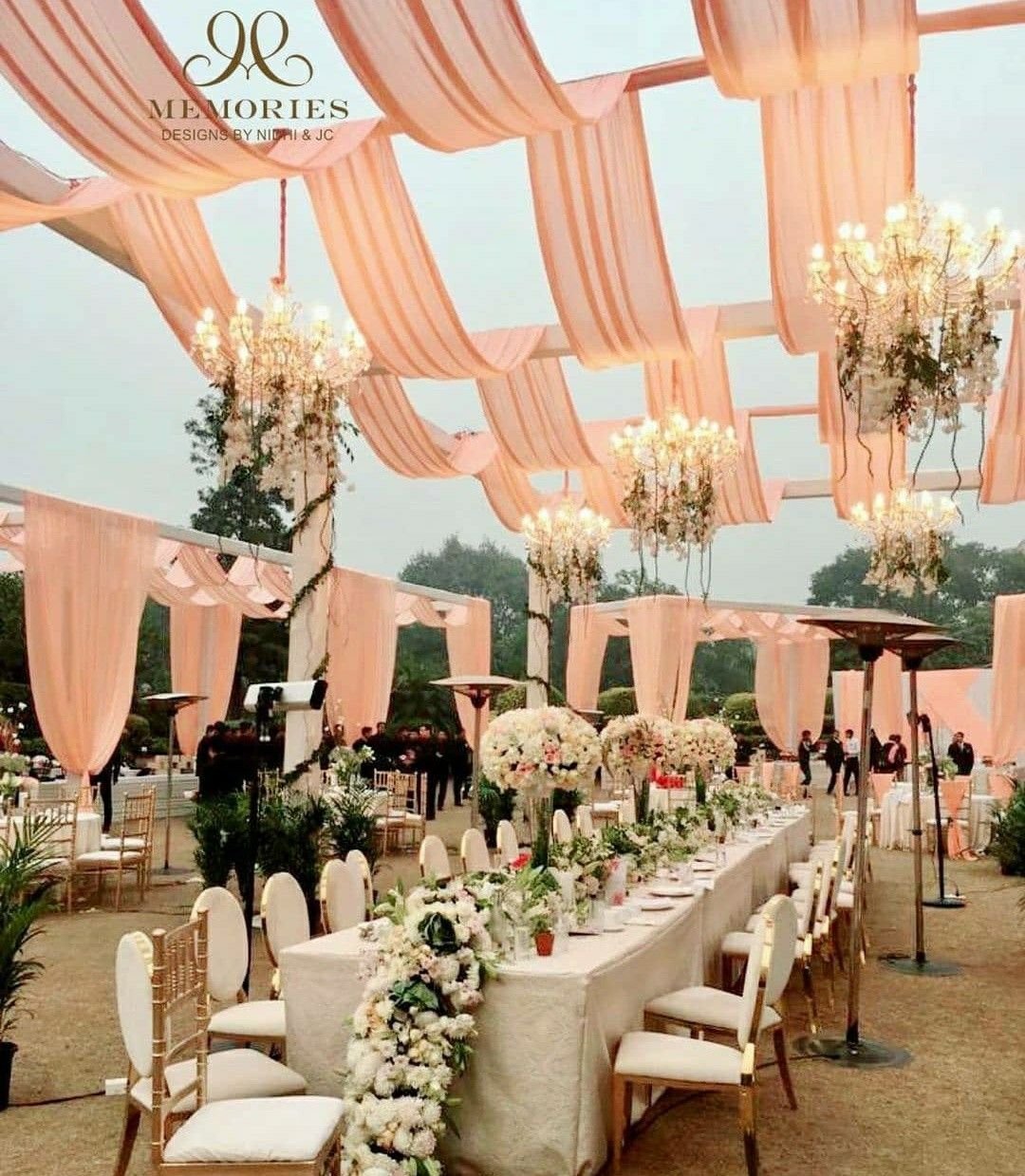 Long banquet table under peach drapes and hanging chandeliers