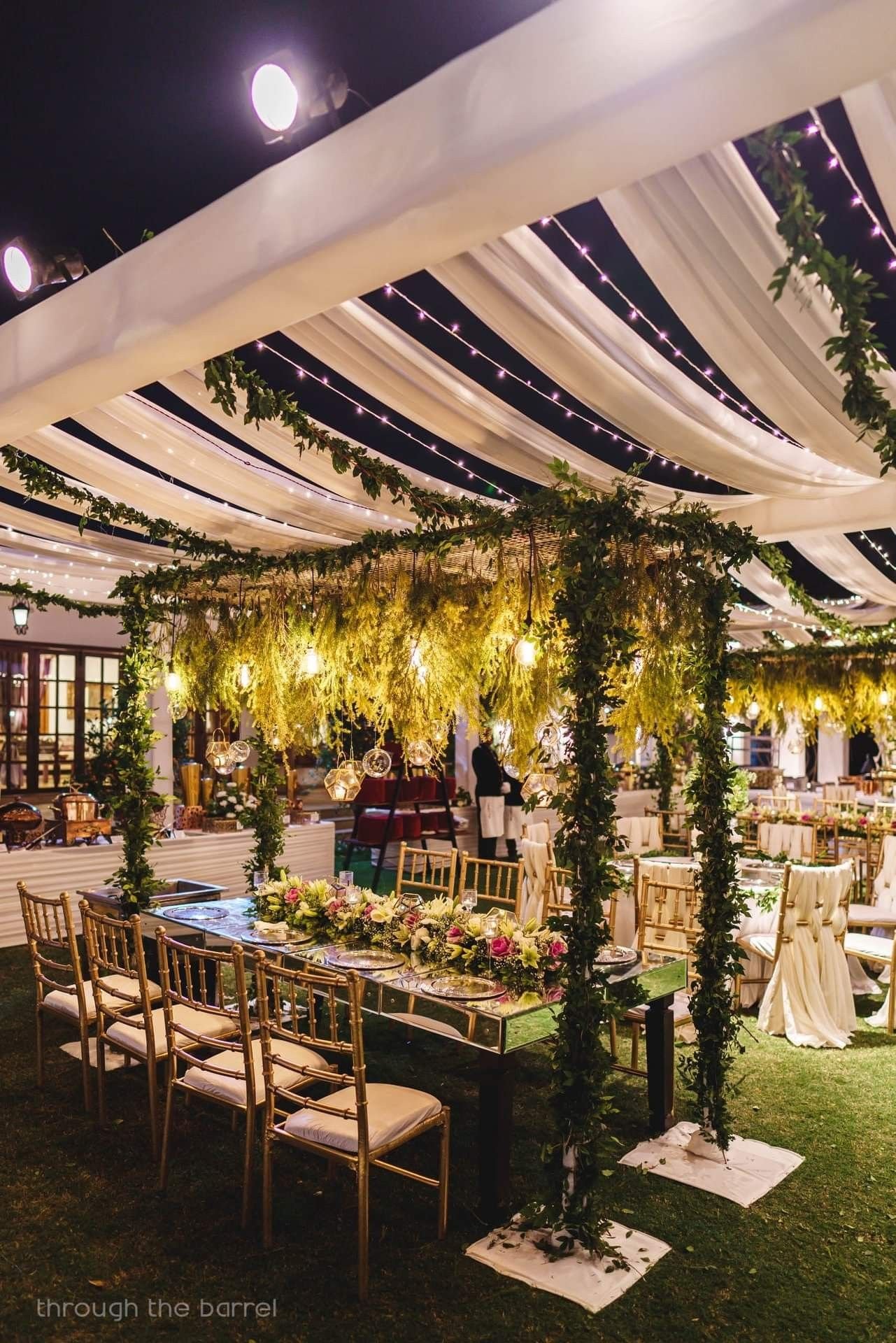 Outdoor dinner table with greenery canopy and string lights at night