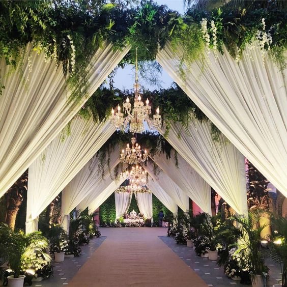 White draped walkway with chandeliers and greenery leading to mandap