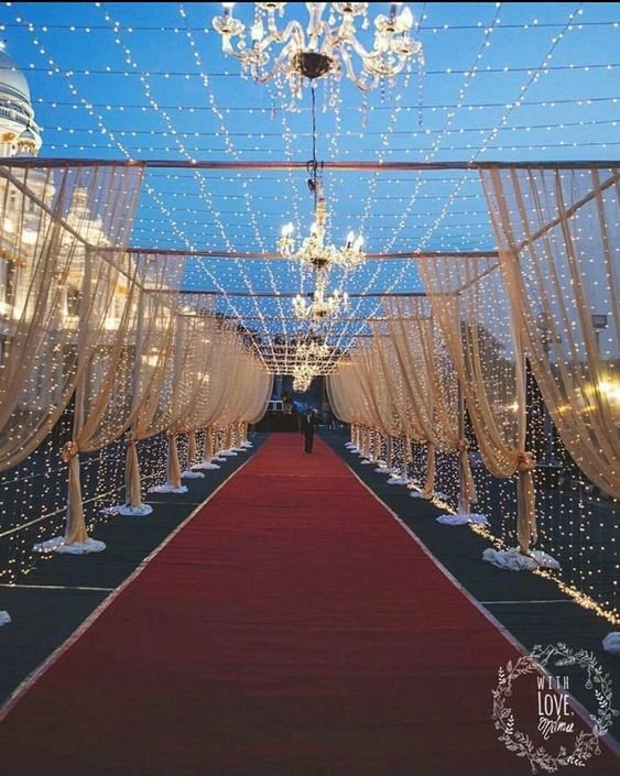 Fairy-light draped aisle with chandeliers leading to a red carpet