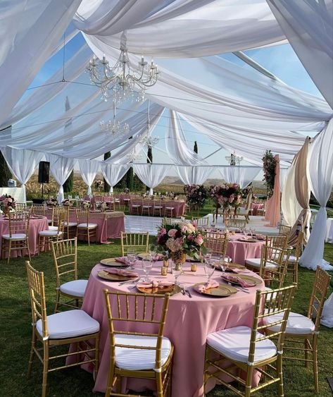 Outdoor pink draped reception tent with round tables and gold chairs