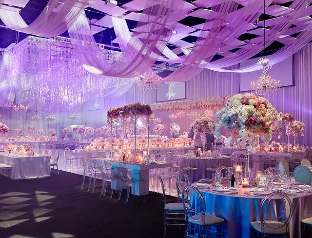 Lavender draped reception hall with chandeliers and floral centerpieces