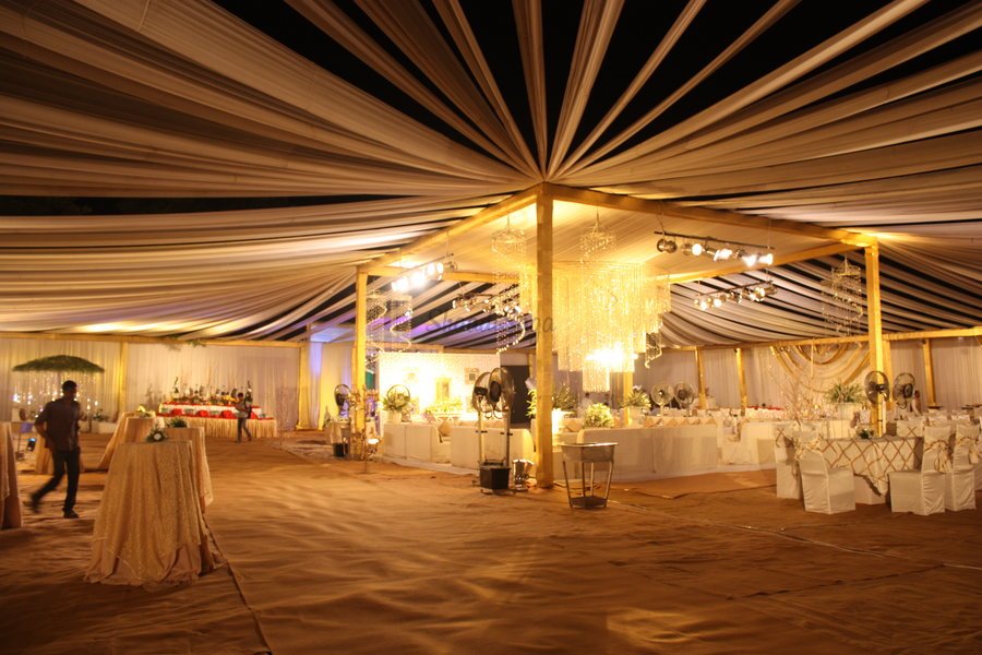 Golden draped reception tent lit at night with chandeliers
