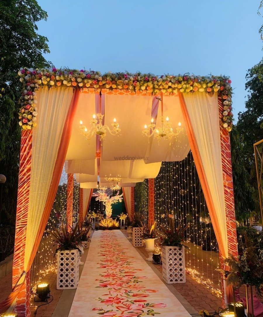Orange and white draped mandap entrance with chandeliers and floral runner